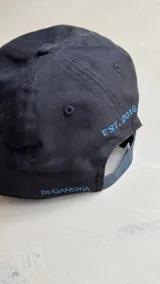 Gorra negra con bordado de las iniciales BG en el frente y diseño de costuras geométricas en la visera.