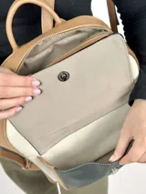 Mochila grande de cuero color beige, blanco y negro charol. Tiene un bolsillo frontal con cierre de broche imantado y logo grabado.