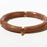 Pulsera rígida de color rosa con vetas blancas, compuesta por segmentos tubulares unidos por anillos dorados. Incluye un dije dorado en forma de gota.