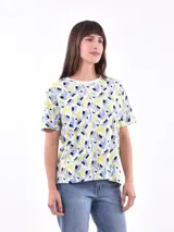 Remera de manga corta color beige con estampado de bananas en tonos amarillo, naranja y rosado.