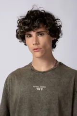Remera de corte holgado con efecto de lavado ácido en tono gris oscuro. Presenta un pequeño estampado gráfico en el centro del pecho con la inscripción 'ASTRAL ENERGY' y las siglas 'VCP'.
