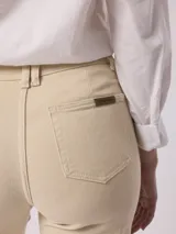 Pantalón jean color beige, de tiro alto y pierna ancha con terminación desflecada.