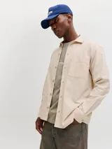 Sobrecamisa de manga larga color beige claro, con cierre frontal de botones, cuello camisero y un bolsillo aplicado en el pecho.