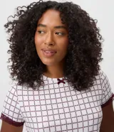 Blusa de pijama de cuello redondo y manga corta, confeccionada en tejido peach touch color blanco con estampado geométrico de corazones en tono bordó. Cuenta con detalles de encaje en los puños y un pequeño moño decorativo en el escote.