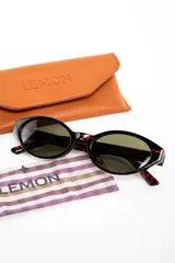 Lentes de sol Lemon de armazón ovalado color negro y cristales oscuros, con detalle de la marca en letras doradas en la patilla.
