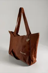 Cartera tipo tote de cuero natural color suela, con diseño envolvente, asas largas de hombro, bolsillo exterior y llavero metálico decorativo con logo.