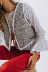 Chaleco corto de paño de lana tejido, con diseño a cuadros en tonos rojo y blanco, ribetes blancos con flecos y cierre frontal mediante lazos de cuero.