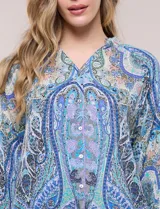 Blusa holgada de poliéster con estampado de arabescos en tonos azules, escote en V con botones frontales, mangas 3/4 y ruedo asimétrico en punta.