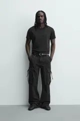 Pantalón cargo de corte relajado en color negro con efecto lavado. Presenta bolsillos laterales tipo cargo con solapas y cintas ajustables, bolsillos frontales y traseros, y detalles de argollas metálicas. Cierre frontal con cremallera y botón.