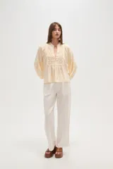 Blusa de viscosa color blanco con diseño holgado, cuello en V y cierre frontal con botones. Presenta detalles de bordado tipo broderie en el frente y en las mangas abullonadas.