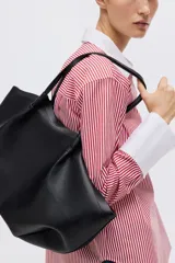 Camisa oversized de popelina de algodón con diseño a rayas verticales rojas y blancas. Presenta cuello clásico y puños anchos en color blanco sólido, cierre frontal con botones y bajo redondeado con aberturas laterales.