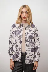 Camisa de manga larga con cuello camisero y cierre frontal de botones. Presenta un estampado floral en tonos oscuros sobre una base de color beige.
