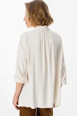 Camisa de corte oversize color chocolate, con cuello clásico, cierre frontal de botones y mangas largas con puños abotonados. Presenta un diseño fluido y holgado con sutiles frunces en los hombros.