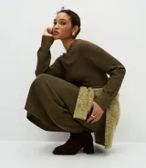 Vestido midi de punto color verde oliva, con cuello redondo y mangas largas. Presenta una textura acanalada y un diseño ajustado que realza la silueta.