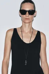 Collar de cordón negro con colgante metálico plateado en forma de pieza de ajedrez (caballo). Cierre con lazada y acabados con piezas metálicas labradas.