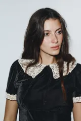 Camisa de terciopelo negro con cuello solapa grande en crochet color crema y detalles de crochet en los bordes de las mangas cortas. Presenta un diseño entallado con cierre de cremallera en la espalda.