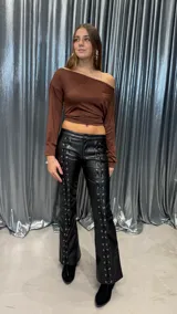 Pantalon de tiro bajo confeccionado en cuero sintetico negro, con diseño de acordonado frontal a lo largo de ambas piernas y corte ligeramente acampanado.