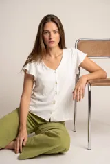 Blusa blanca con escote en V, mangas cortas con volados y cierre frontal con botones.