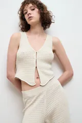 Chaleco de punto color crudo, con escote en V y cierre frontal con ganchos metálicos.