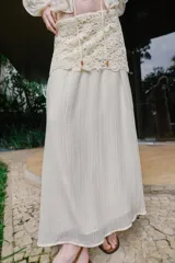 Falda midi de color crudo, con diseño combinado que presenta una parte superior de crochet con motivos florales y una parte inferior de tela fluida con textura arrugada. Incluye forro interior y cierre lateral con cremallera oculta.