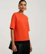 Blusa básica de mujer color negro, confeccionada en malla encorpada de algodón, con cuello redondo y mangas cortas de corte oversized con sisas desplazadas.