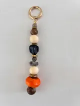 Colgante decorativo para bolso o llavero, compuesto por una cadena metálica con un conjunto de cuentas de diferentes formas, colores y texturas, incluyendo piedras naturales y cuentas de madera.