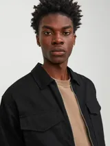 Campera negra de manga larga con cuello camisero y cierre frontal con cremallera. Tiene dos bolsillos de parche con solapa abotonada en el pecho.