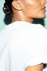 Remera blanca de manga corta y cuello redondo, con un estampado gráfico que simula una postal de Brasil, mostrando una playa tropical con palmeras y vegetación.