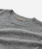Suéter de punto color beige con cuello redondo, manga larga y aplicaciones de perlas distribuidas por toda la prenda. Presenta puños y ruedo acanalados.