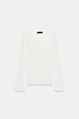 Chaqueta de punto rib color blanco, con cuello redondo, manga larga con acabado ondulado en los puños y cierre frontal con botones.