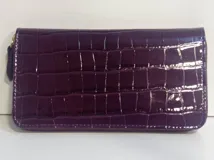 Billetera rectangular con cierre perimetral, confeccionada en cuero con textura de reptil y acabado brillante. Cuenta con múltiples compartimentos internos para tarjetas, documentos y billetes, además de un bolsillo interno con cierre para monedas.