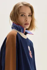 Sweater de tejido de punto azul marino con mangas raglan en color camel y puños con detalles en rojo y beige. Presenta un aplique bordado en el pecho con motivos de fantasía.