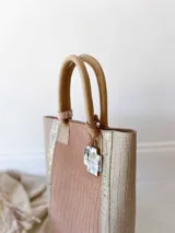 Bolso matero de cuero color beige y nude con textura croco. Tiene doble asa de mano color cuero y dije colgante con forma de cruz. No tiene división interna y se le puede agregar una correa larga opcional.