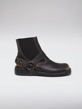 Bota de cuero color marrón oscuro con punta cuadrada, diseño tipo chelsea con paneles elásticos laterales y estribo decorativo con hebilla metálica ajustable.
