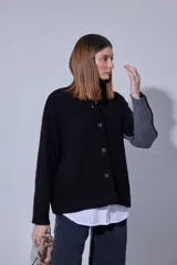 Saco de punto acanalado en color gris claro, con cierre frontal de botones oscuros. Presenta un diseño de bloques de color en las mangas, combinando negro y marrón, y un cuello redondo.