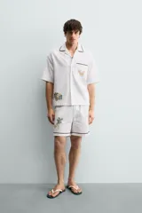 Camisa de corte relajado confeccionada en algodón, con cuello bowling y manga corta. Presenta un bolsillo en el pecho con vivo a contraste y bordados decorativos en el frente. Cierre frontal mediante botones.