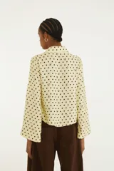 Blusa de lunares color amarillo con diseño de puntos y detalles oscuros, cuello camisero y cierre frontal con cordones para atar.