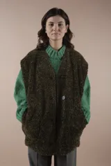 Chaleco largo acolchado color verde oliva, reversible con un lado de piel sintética y otro de pelo sintético. Tiene cuello en V, cierre con botones a presión y bolsillos laterales. Silueta amplia y relajada.