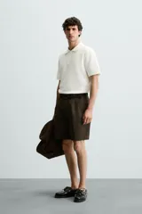 Polo de manga corta color blanco roto, con cuello solapa y cierre frontal de cremallera. Presenta un tejido de piqué estructurado y corte regular fit.