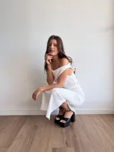 Conjunto de dos piezas en color blanco, compuesto por un top con escote bote y hombros descubiertos, y una falda midi con tajo lateral. Ambas prendas están confeccionadas en tela bambula elastizada con textura arrugada.