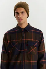 Camisa de franela a cuadros azul marino, marrón y naranja, de corte recto, manga larga, con dos bolsillos frontales con solapa abotonada y cierre frontal con botones.