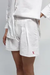 Short de tiro medio confeccionado en algodón tussor, de color blanco con costuras a la vista en color rojo. Presenta tablones delanteros que aportan volumen y un pequeño bordado con la letra V en el ruedo.
