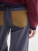 Pantalón jean de tiro alto y corte pinzado, con perneras de caída suelta y levemente anchas en el bajo. Posee pasador con hebilla en la parte trasera.