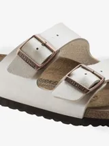 Sandalia Birkenstock modelo Arizona de dos tiras, color blanco nacarado brillante. Presenta hebillas ajustables de metal color cobre y plantilla anatómica de corcho-látex forrada en ante.