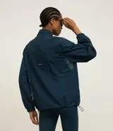 Campera deportiva tipo cortavientos en color azul petróleo, con cuello alto y cierre frontal completo. Presenta recortes de tul translúcido en los laterales, puños elásticos y bolsillos funcionales. Confeccionada en tejido de poliamida.