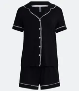 Conjunto de pijama corto negro con ribetes blancos, compuesto por una camisa de manga corta con cuello, bolsillo en el pecho y cierre abotonado, y un short con cintura elástica.