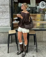 Buzo tejido de punto en color marrón chocolate, con diseño off-shoulder, cuello amplio y mangas largas con puños acanalados. Presenta una textura acanalada y un calce relajado.
