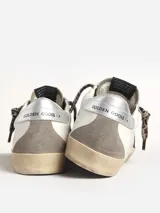 Zapatillas Golden Goose modelo Super-Star, con pala de cuero blanco, estrella con purpurina color burdeos, refuerzo del talón de piel laminada plateada, aplicaciones de ante gris paloma y cordones con estampado de leopardo en tonos beige y marrón.