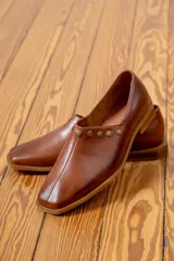 Zapato de cuero vacuno color negro, con punta cuadrada y detalle de tachas metálicas planas en el borde superior. Presenta costura central en el empeine y taco geométrico.