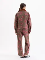 Pantalon de corte recto y tiro medio, confeccionado en tela color marrón con estampado de fresas y hojas en tono rosado. Cuenta con cierre frontal y bolsillos laterales.